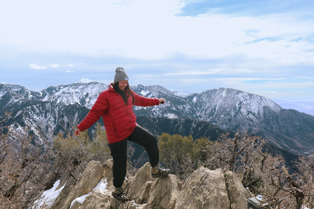 Melanie hiking on a rocky mountain summit above snow-capped peaks